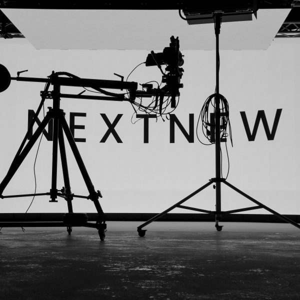 A camera crane and lighting rig silhouetted against a lit cyclorama on set